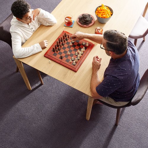 two people playing chess at a wooden table in a room with purple carpet from Carpet Design Center in the Greenville, NC area